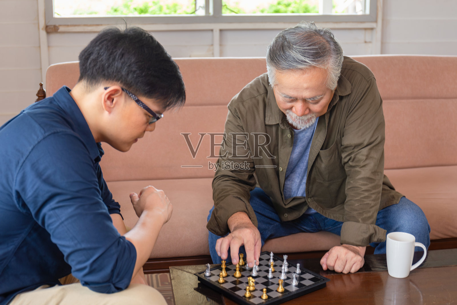 亚洲老年父亲和中年儿子在客厅下棋，幸福亚洲家庭理念照片摄影图片