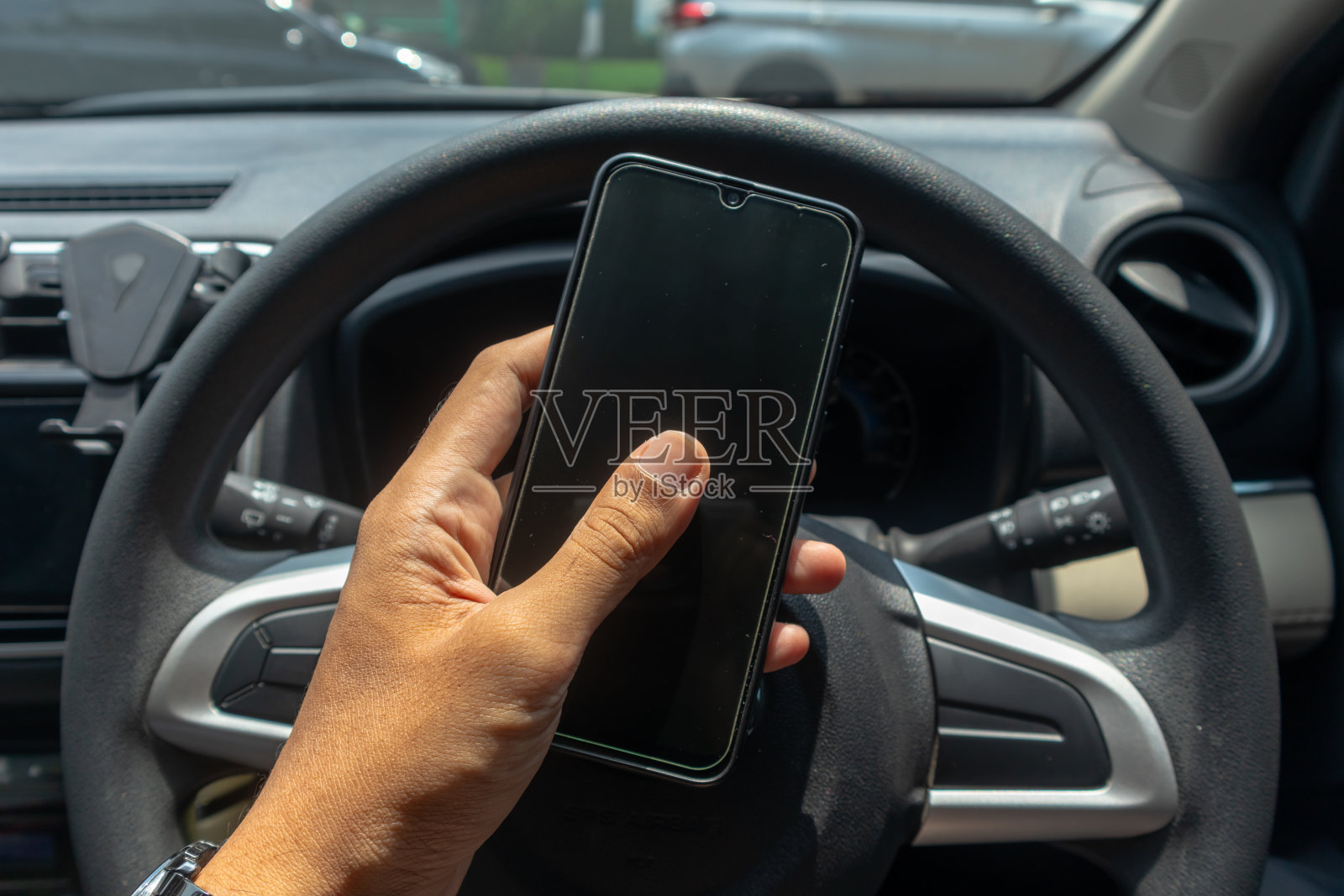 男性手持智能手机，背景是汽车方向盘。驾驶时使用智能手机的概念。照片摄影图片
