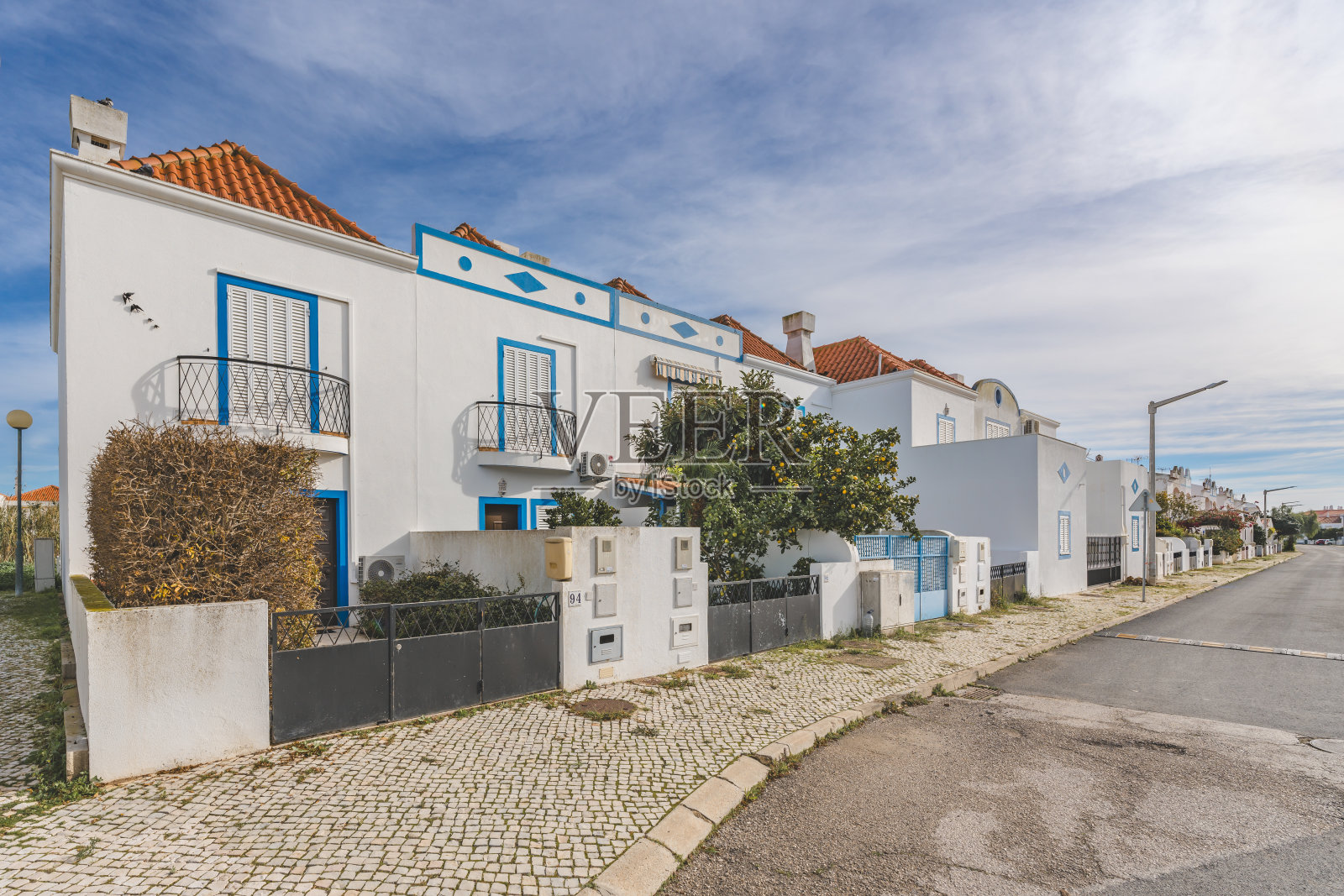 葡萄牙曼塔罗塔的一个安静的住宅区，重点是一座有拱门的白色房子，一个围起来的庭院和一条鹅卵石人行道。照片摄影图片