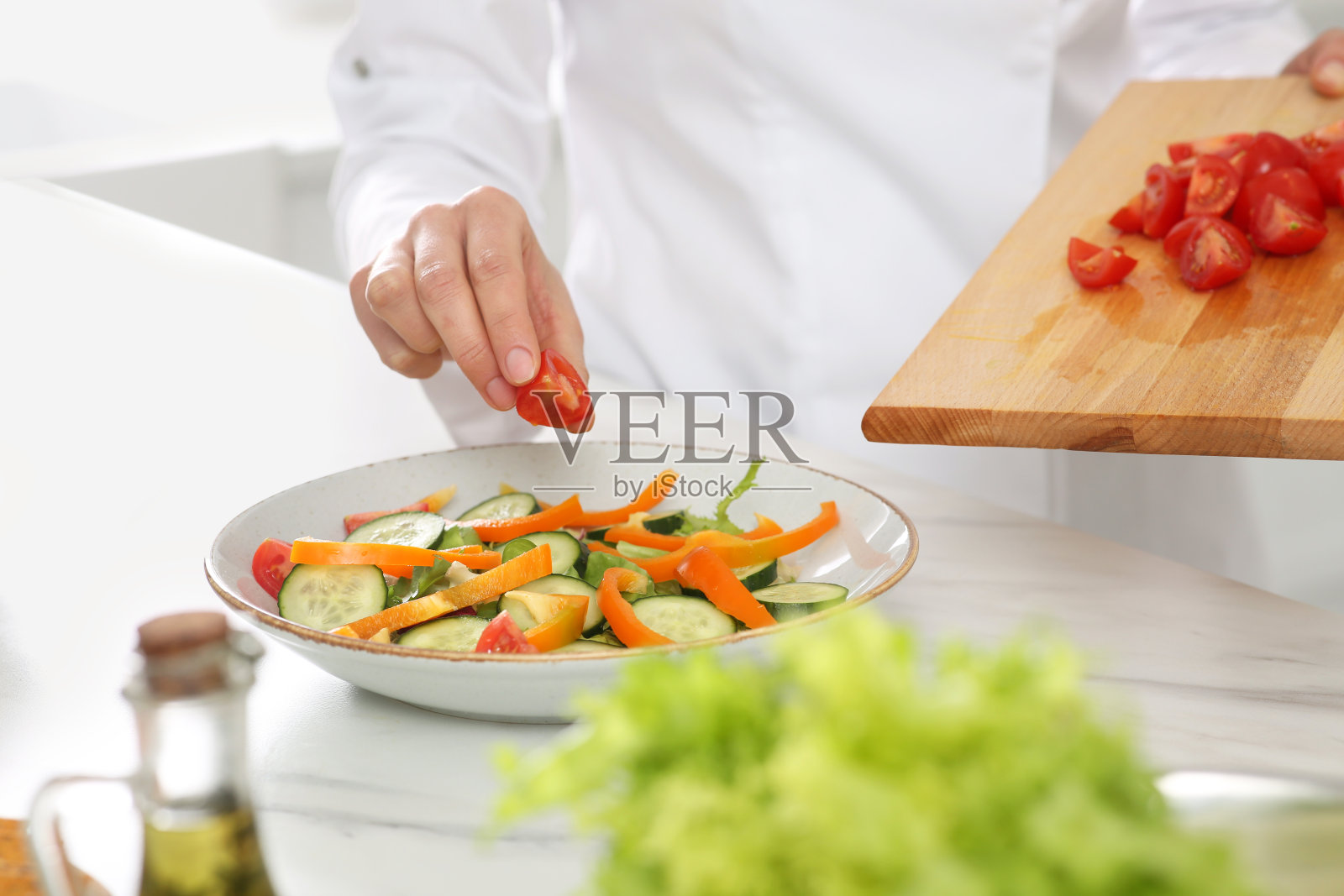 专业厨师在白色大理石餐桌上把切好的番茄加入美味的沙拉中，特写照片摄影图片