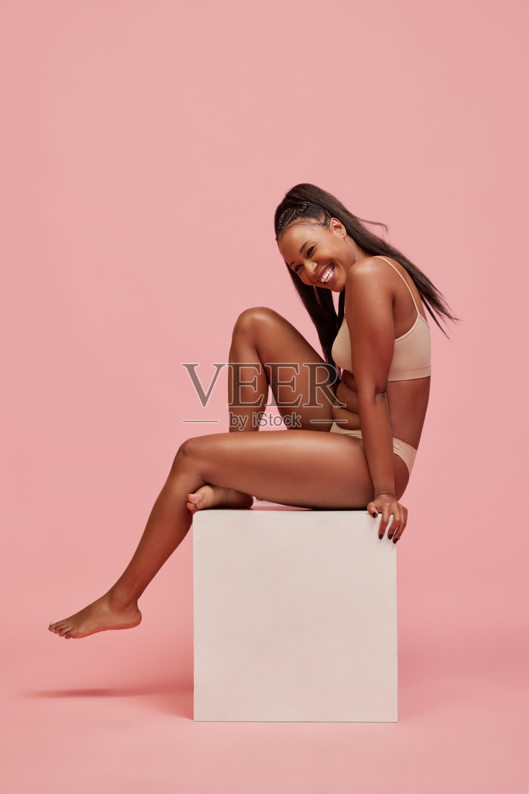 美丽，微笑的年轻非洲女人，长头发，穿着内衣，在粉红色的工作室背景下摆姿势。多民族的美照片摄影图片