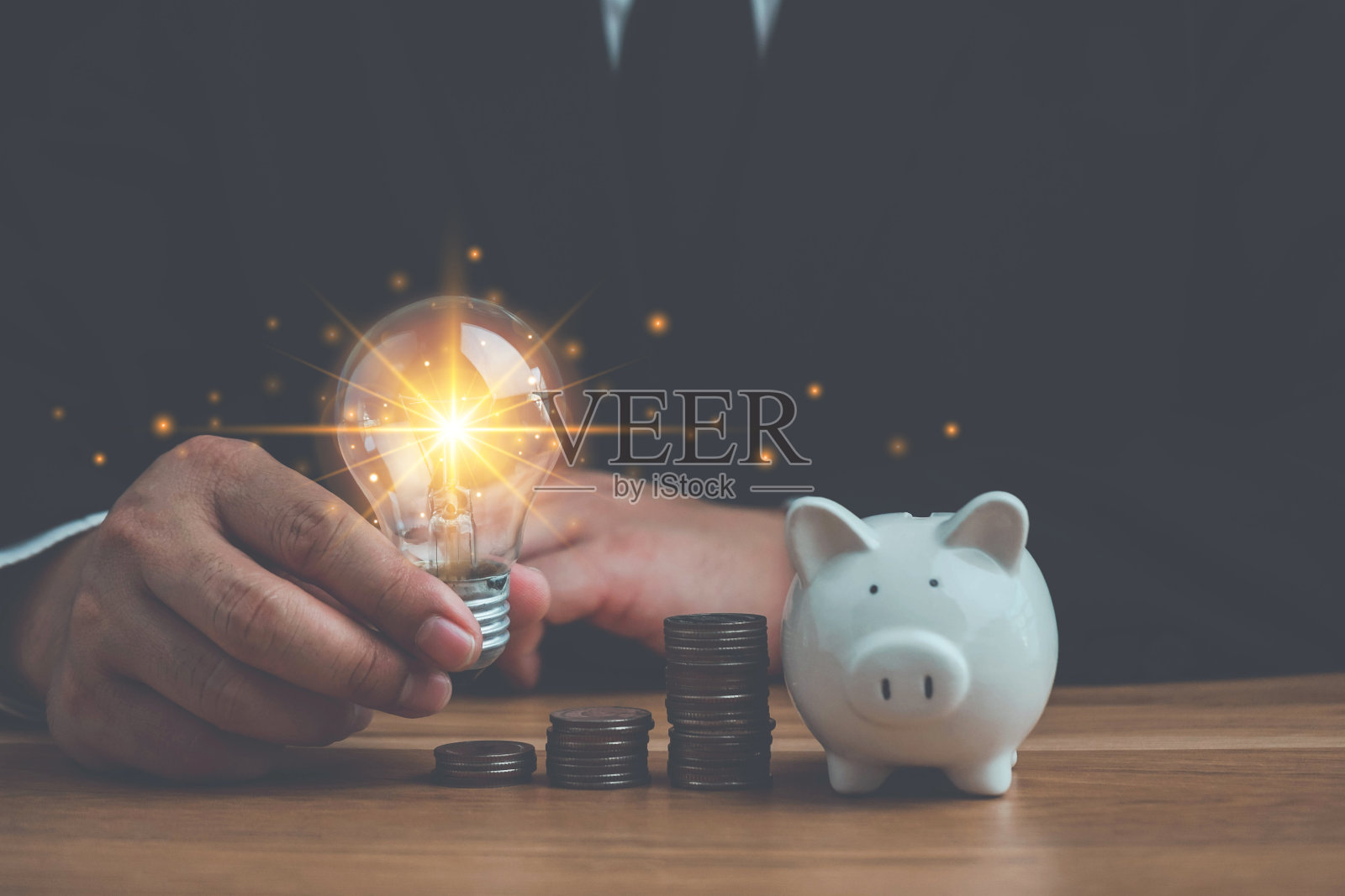 商务男士手持灯泡和硬币堆放在办公桌上，省钱理财理念，居家理财理念，节约能源和会计理财理念，节约能源和电力。照片摄影图片