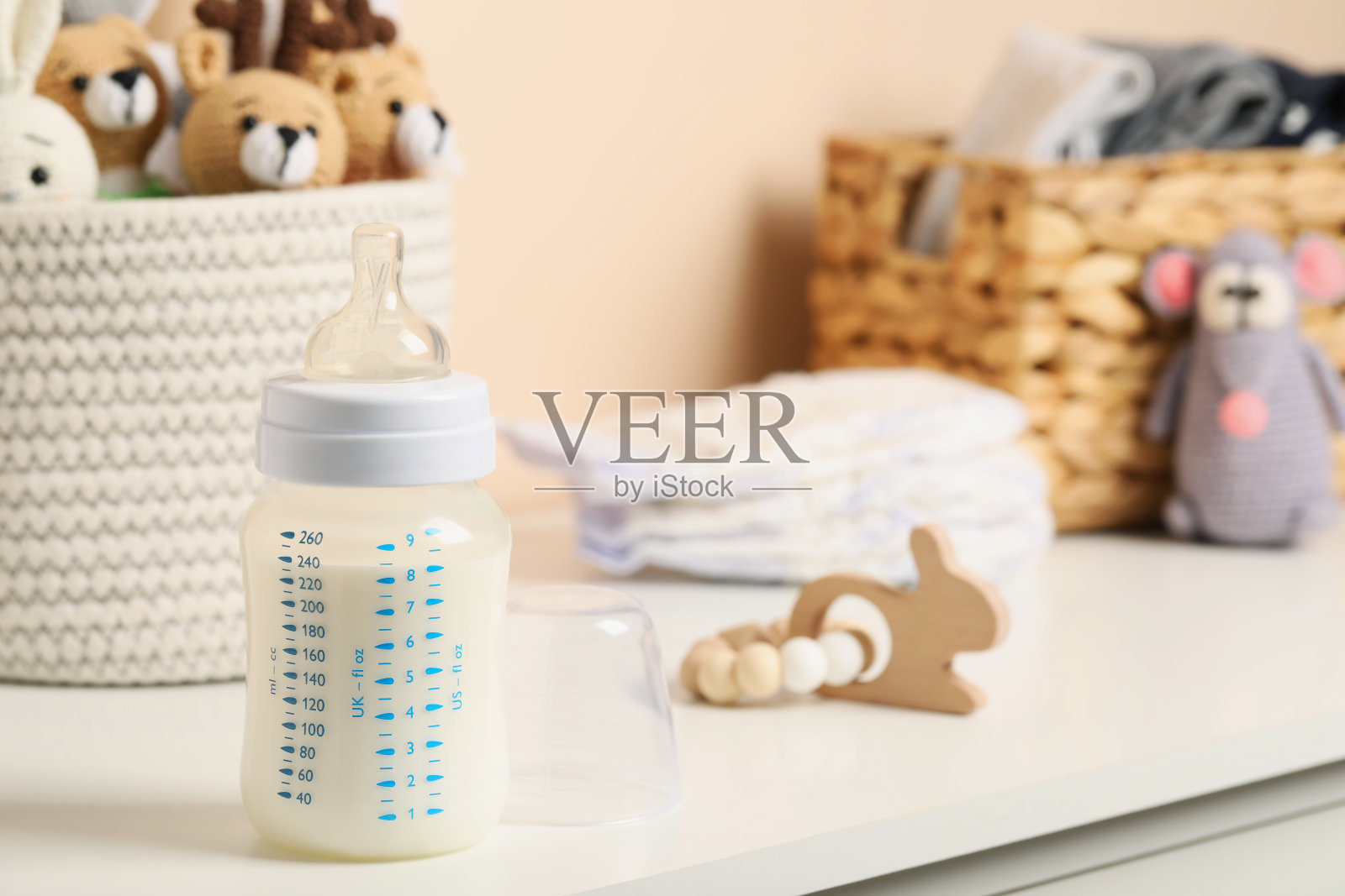 靠近米色墙壁的白色桌子上放着装有牛奶的奶瓶和其他婴儿用品。文本空间照片摄影图片
