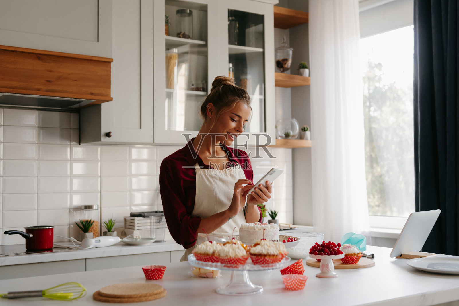 快乐的年轻女糖果师在家庭厨房用智能手机做蛋糕照片摄影图片