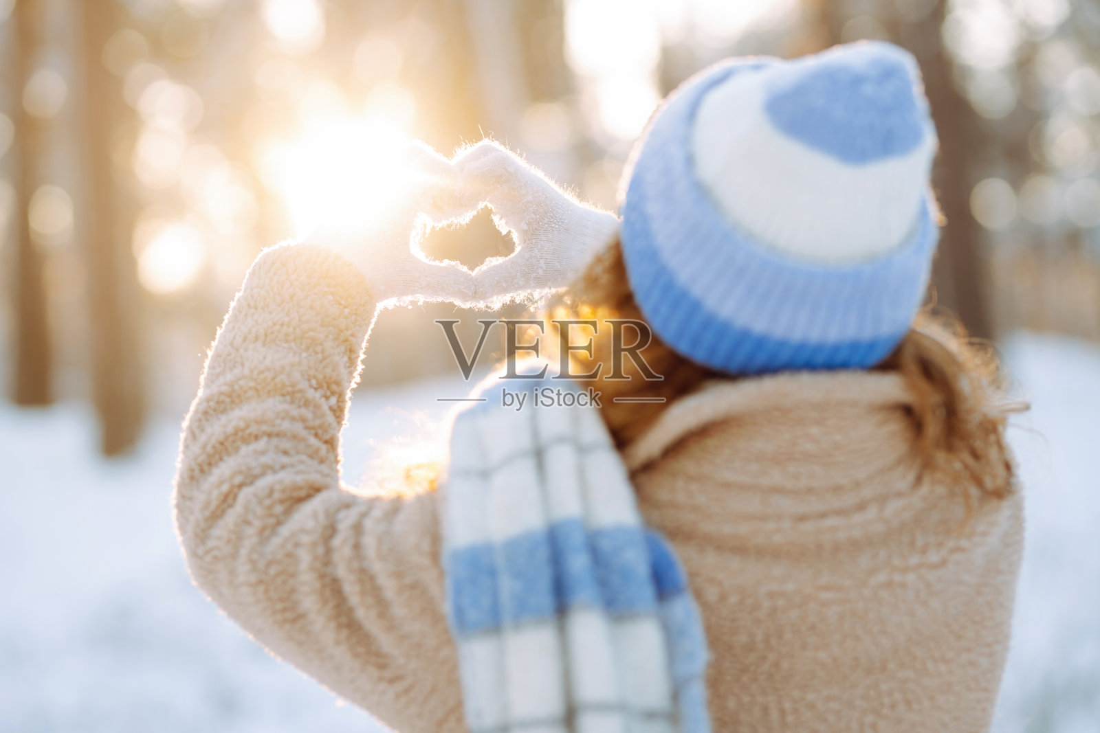 在白雪皑皑的冬季森林背景下，一位戴着帽子、围着围巾的妇女双手握成心形。照片摄影图片