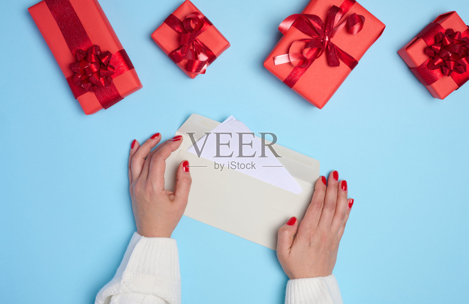 女性双手拿着一个蓝色背景的白色信封，周围是一个装有礼物的盒子照片摄影图片