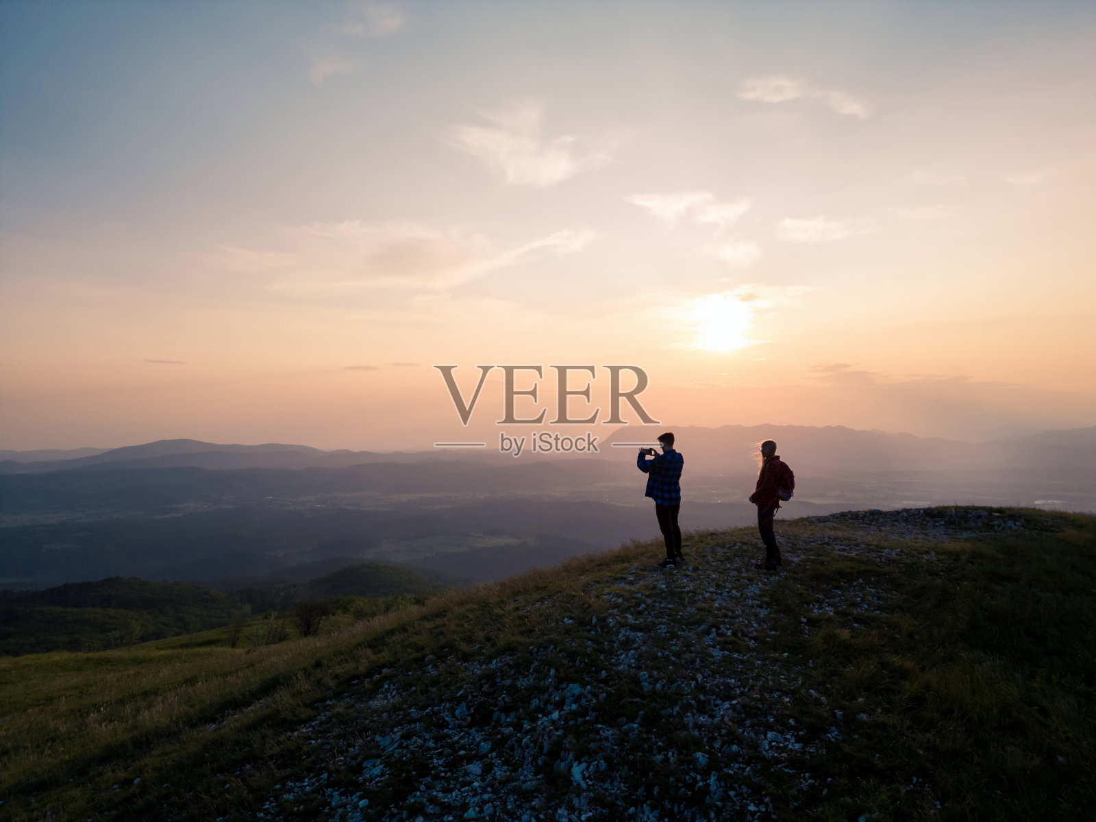 少年在一个背着背包的女孩的陪伴下拍摄日落照片摄影图片