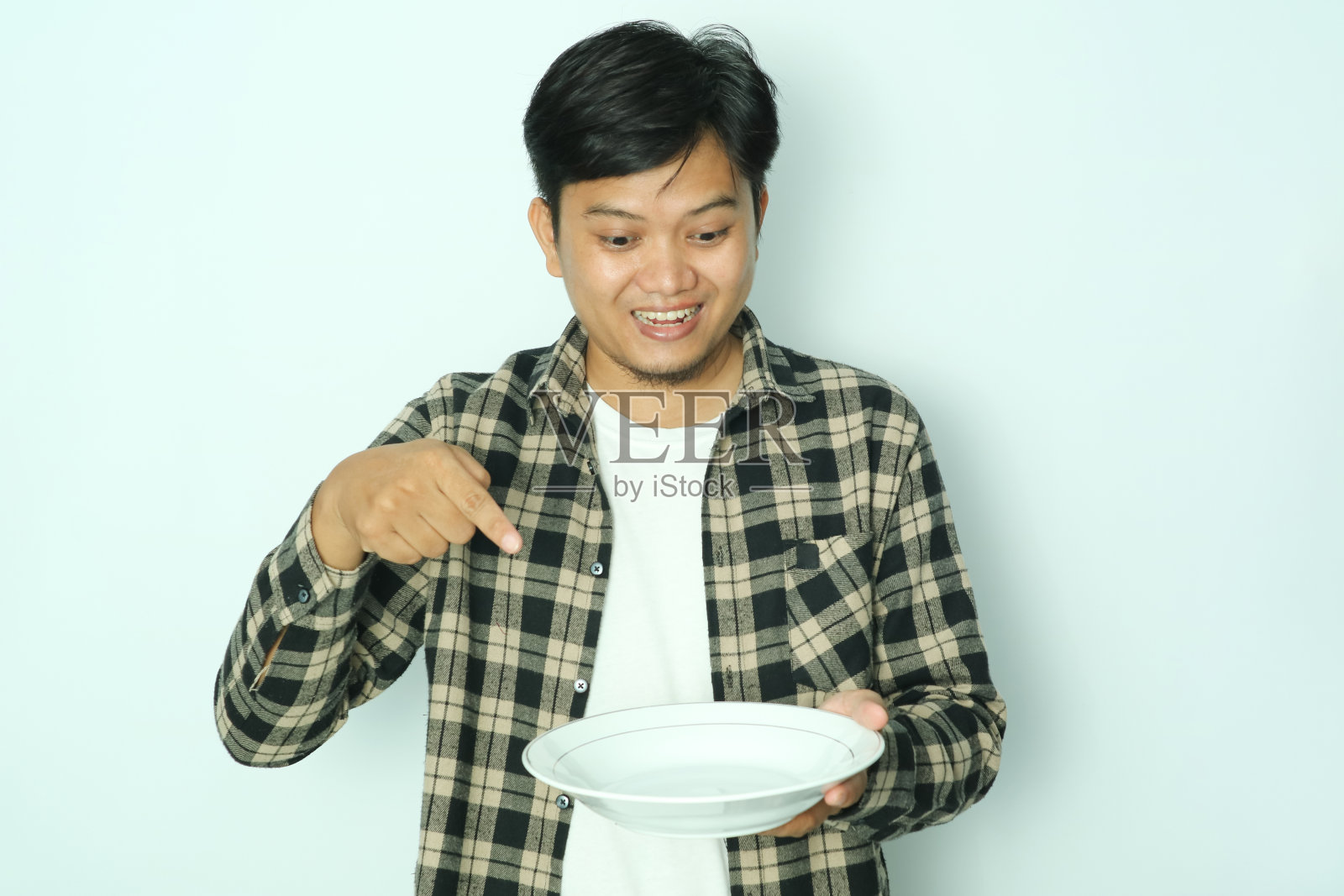 年轻的亚洲男子开心地笑着，指着他手里的空盘子照片摄影图片