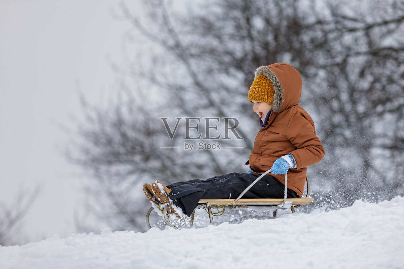 戴着针织帽的快乐小孩的肖像。小男孩在冬天的风景中享受雪橇。孩子在雪中乘坐雪橇。冬天编织孩子的衣服和连指手套照片摄影图片
