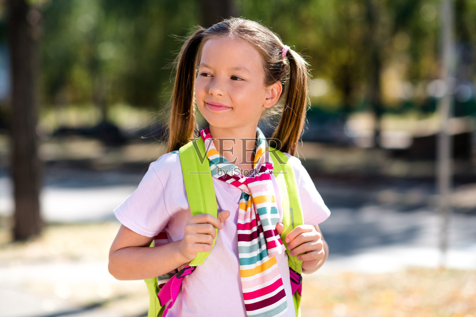 梦幻甜美的小女孩穿着系好的套头毛衣背包在城市公园外散步上学照片摄影图片