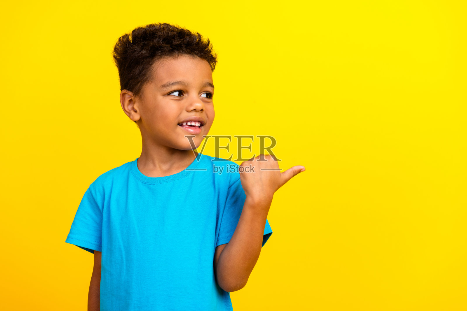可爱的男学生的肖像，留着非洲式发型，穿着蓝色t恤，在生动的黄色背景上看着广告空白的空间照片摄影图片