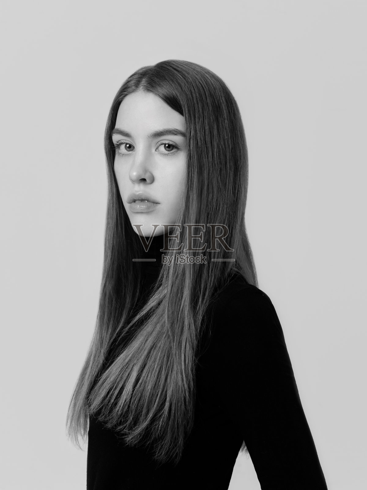 年轻女子与迷人的大眼睛看着相机时尚模特长直发黑色穿着高领毛衣，但看起来优雅感性和性感的同时工作室肖像在浅色背景前视图特写镜头脆弱漂亮的生物照片摄影图片