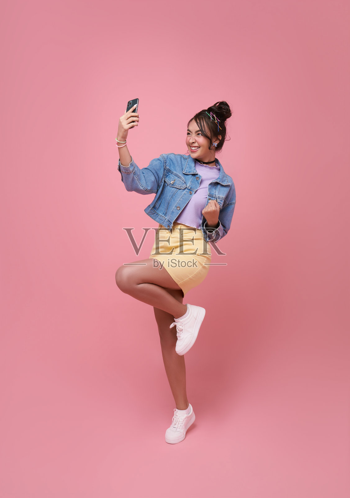 一个快乐的年轻亚洲女性的肖像，她在粉红色的背景下用手机庆祝。照片摄影图片