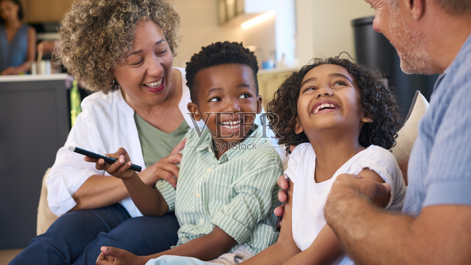 祖父母和孙子坐在家里的沙发上看电视，背后是父母照片摄影图片