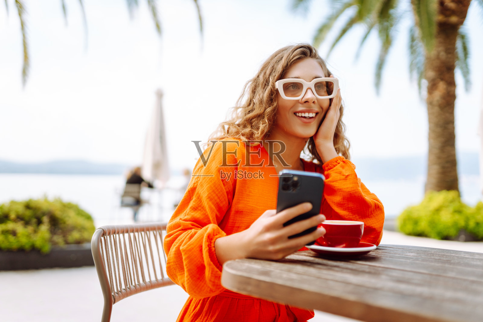 坐在夏日咖啡馆边喝咖啡边玩手机的快乐女人的画像。照片摄影图片