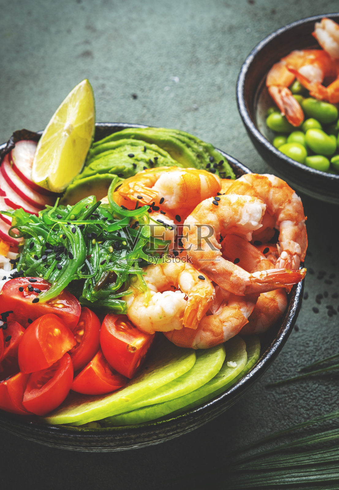 以虾、米饭、鳄梨、蔬菜和chuka沙拉为平衡饮食的Poke bowl，绿色桌面背景，俯视图照片摄影图片