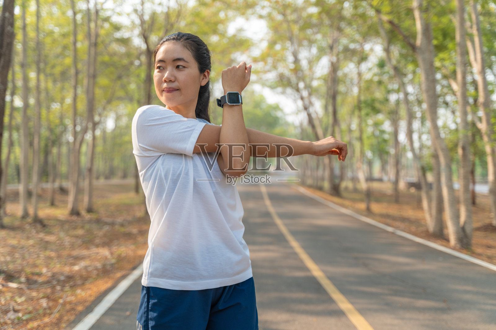 在当地的一个跑步公园，年轻的女跑步者在开始晨跑前伸展胳膊和腿照片摄影图片