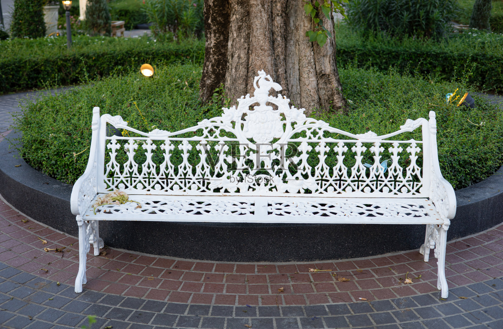 花园的树下放了一张白色的长凳。照片摄影图片