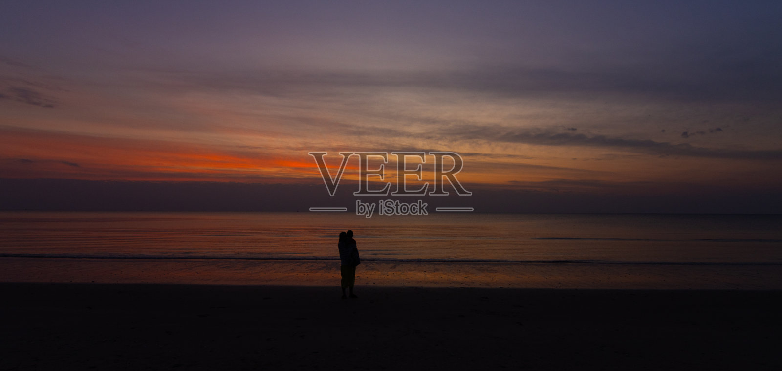 黑暗的母亲抱着婴儿在沙滩上与日落自然海岸景观夏天照片摄影图片