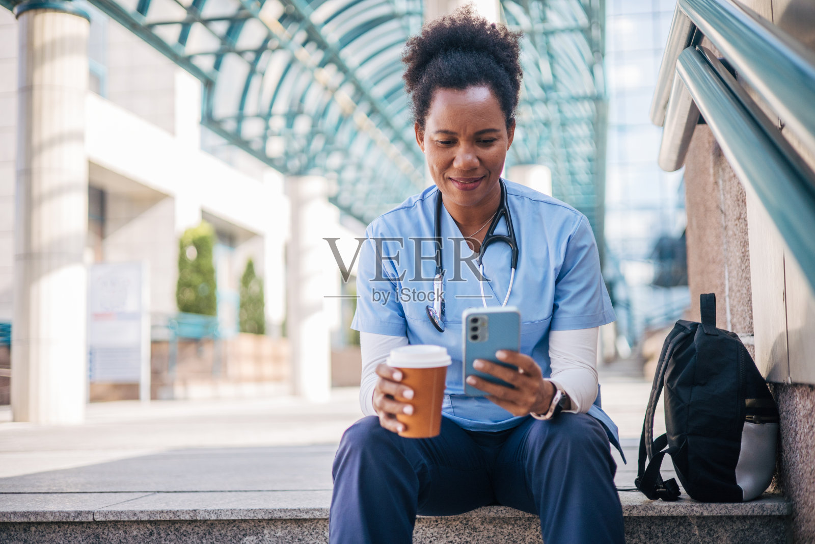 一名女卫生工作者坐在户外，一边用智能手机一边喝咖啡照片摄影图片