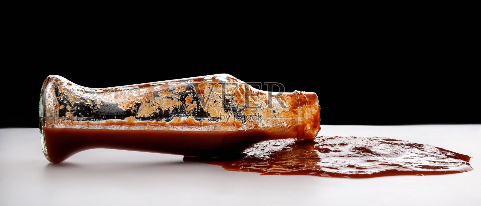 番茄酱。一个装着番茄酱的玻璃瓶，周围洒了一滩番茄酱。照片摄影图片