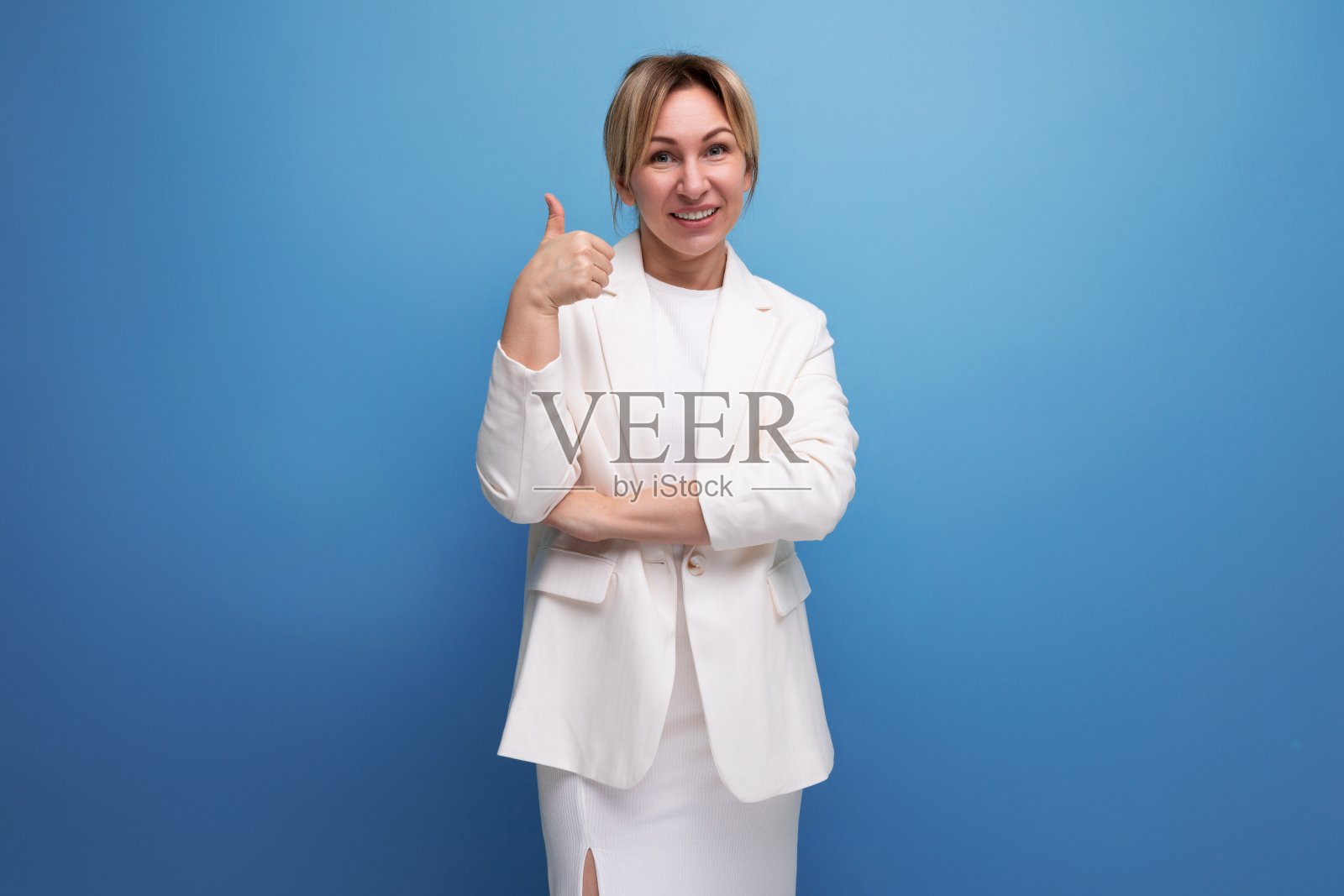 年轻自信，漂亮苗条的金发女老板穿着优雅的夹克和裙子，蓝色背景与复制空间照片摄影图片
