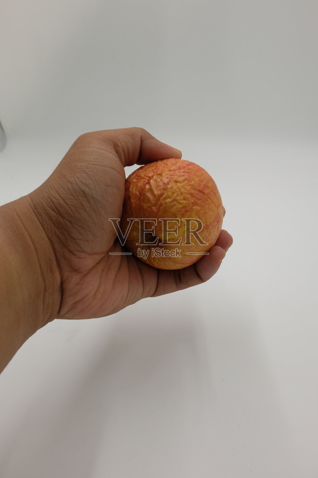 一个人的手拿着一个枯萎的苹果，孤立在白色的背景上照片摄影图片