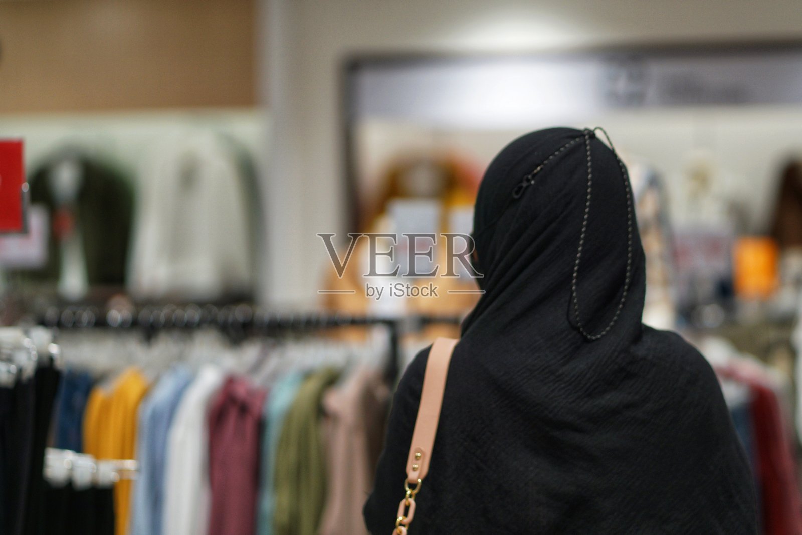 漂亮的年轻亚洲妇女戴着头巾在购物中心看服装产品。漂亮快乐的女孩在商场中心的衣架上挑选新衣服和t恤。照片摄影图片