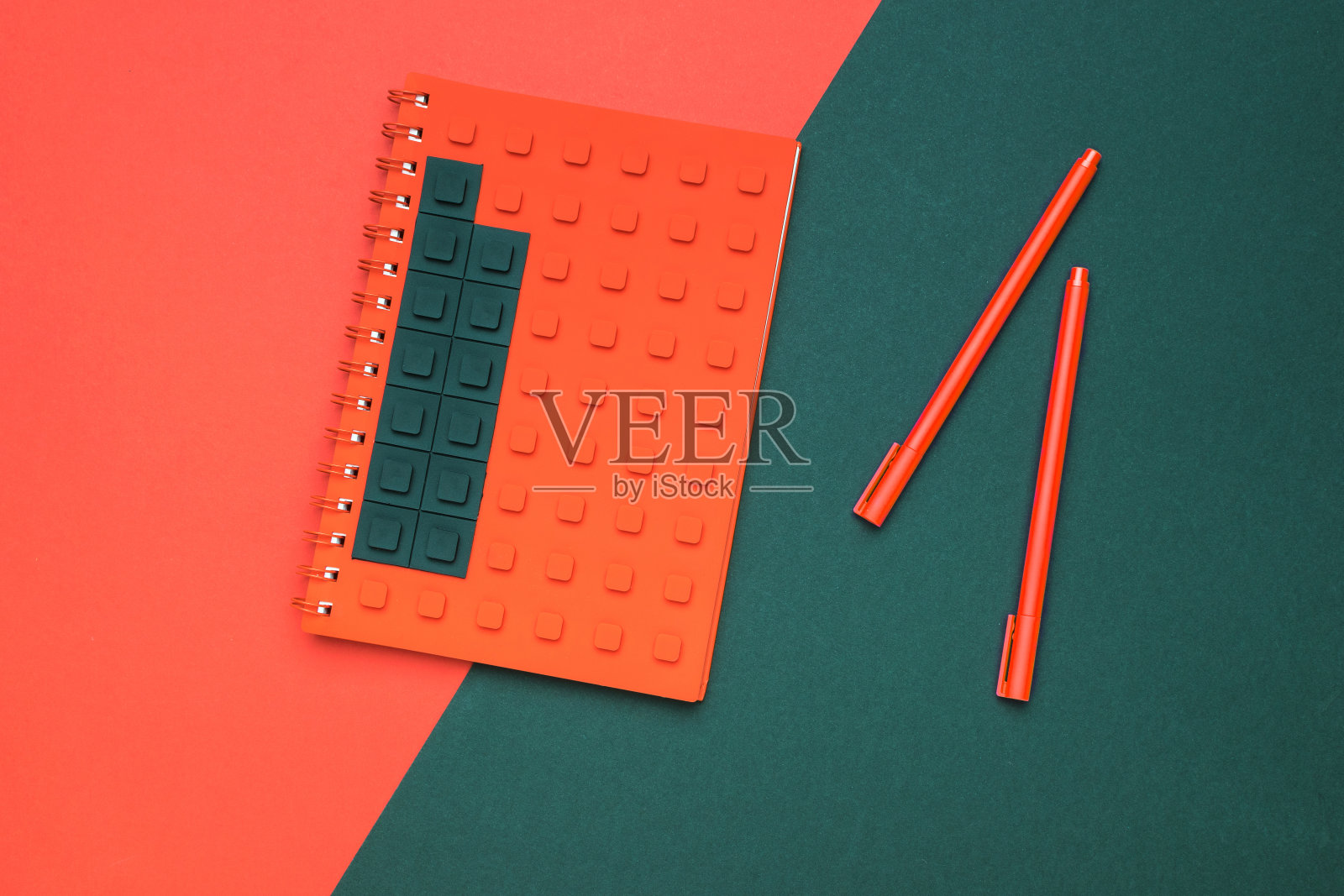 一个笔记本，有一个创意的封面和两支笔，在红黑背景上。照片摄影图片