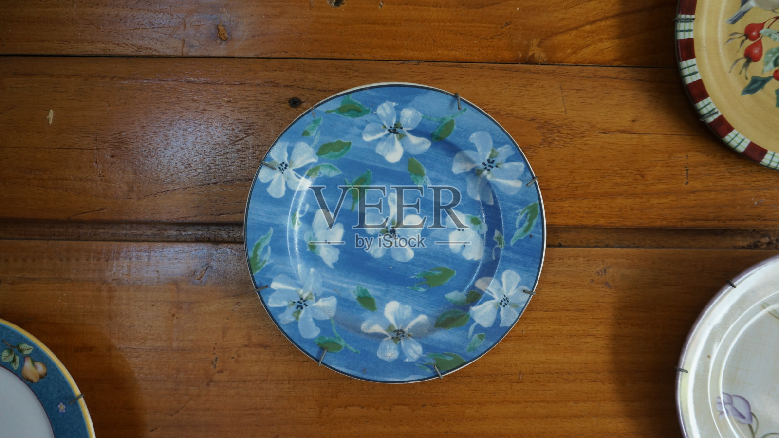 挂在木墙上，蓝边饰有白花画的蓝色装饰板照片摄影图片