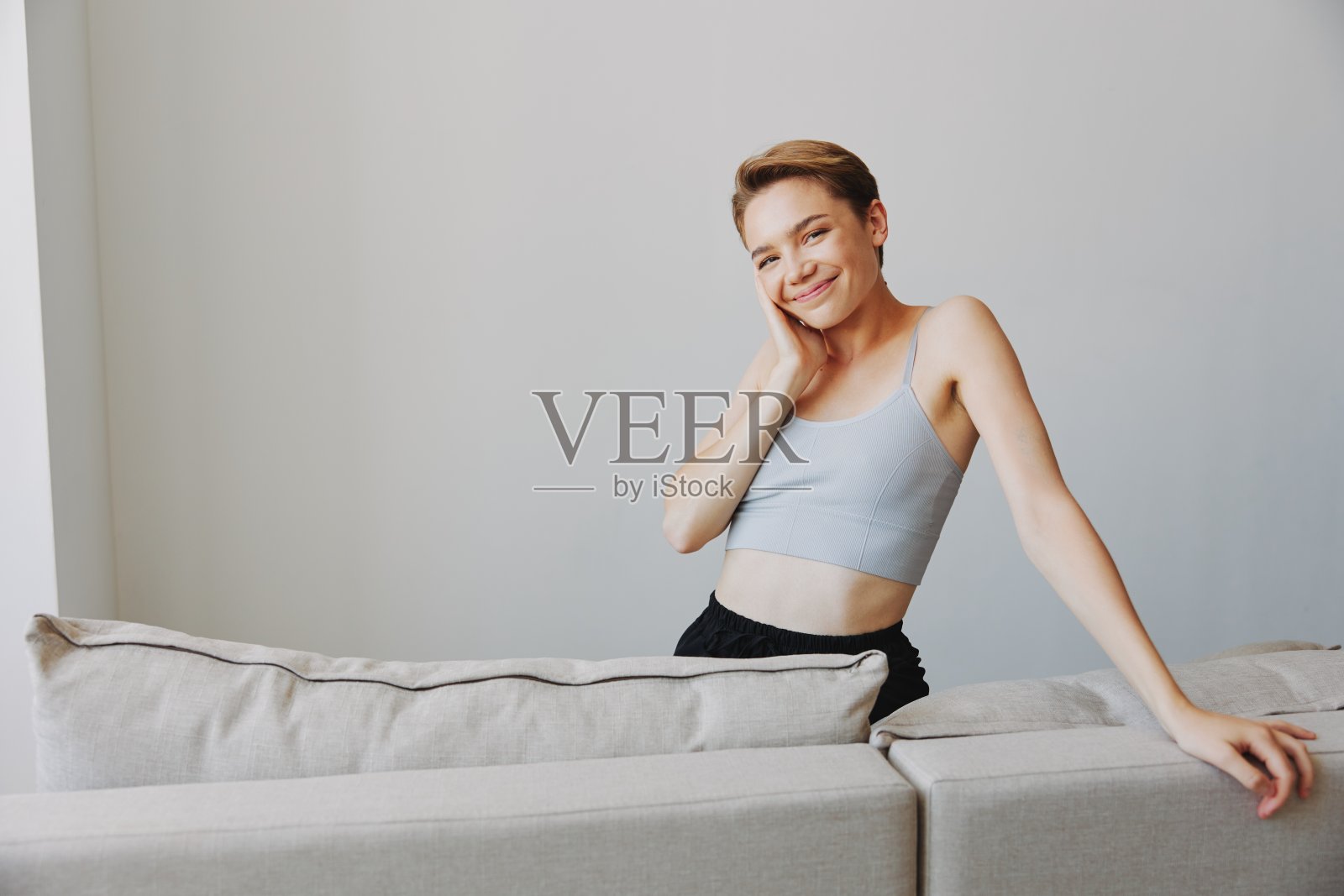 快乐的女人微笑着躺在家里的沙发上，周末在家放松，短发，白色背景，没有过滤器的头发，自由的复制空间照片摄影图片