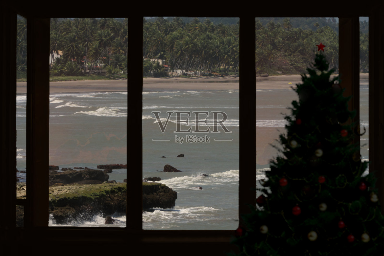 这是一幅蒙太奇照片，窗户旁边有一棵圣诞树的剪影，背景是阿拉戈斯海岸的景色，将南半球国家的圣诞节庆祝活动概念化，照片摄影图片