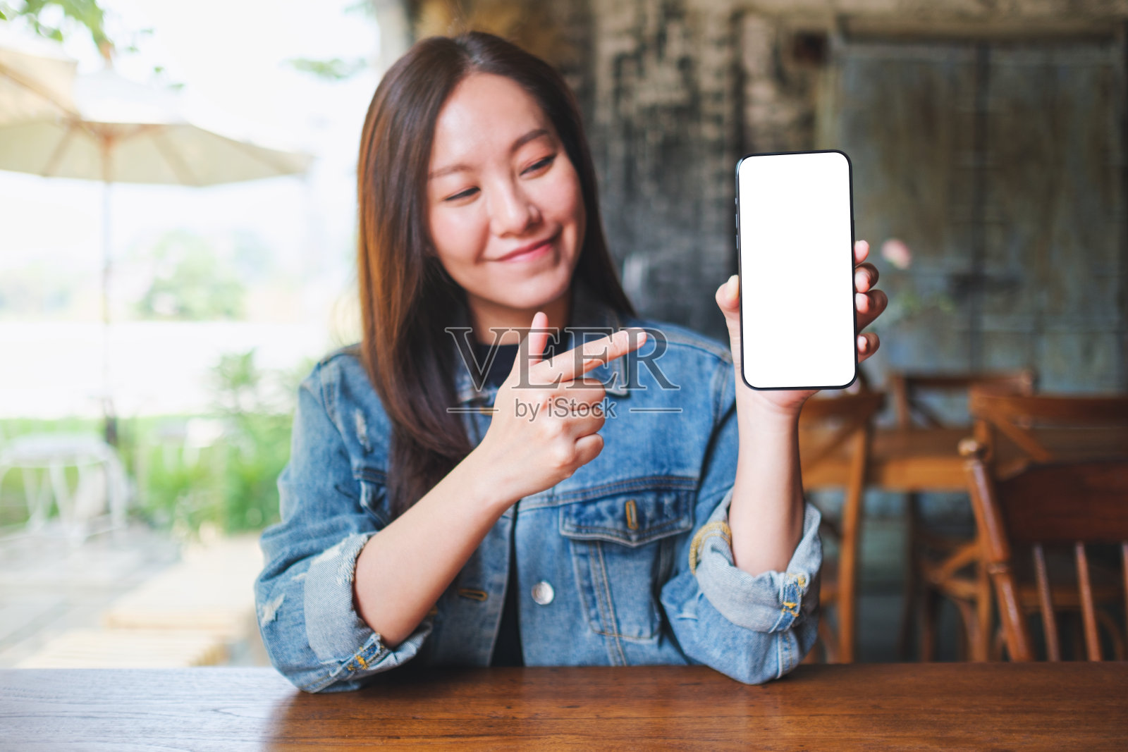 一个年轻女子拿着手机，手指着手机，屏幕是空白的照片摄影图片