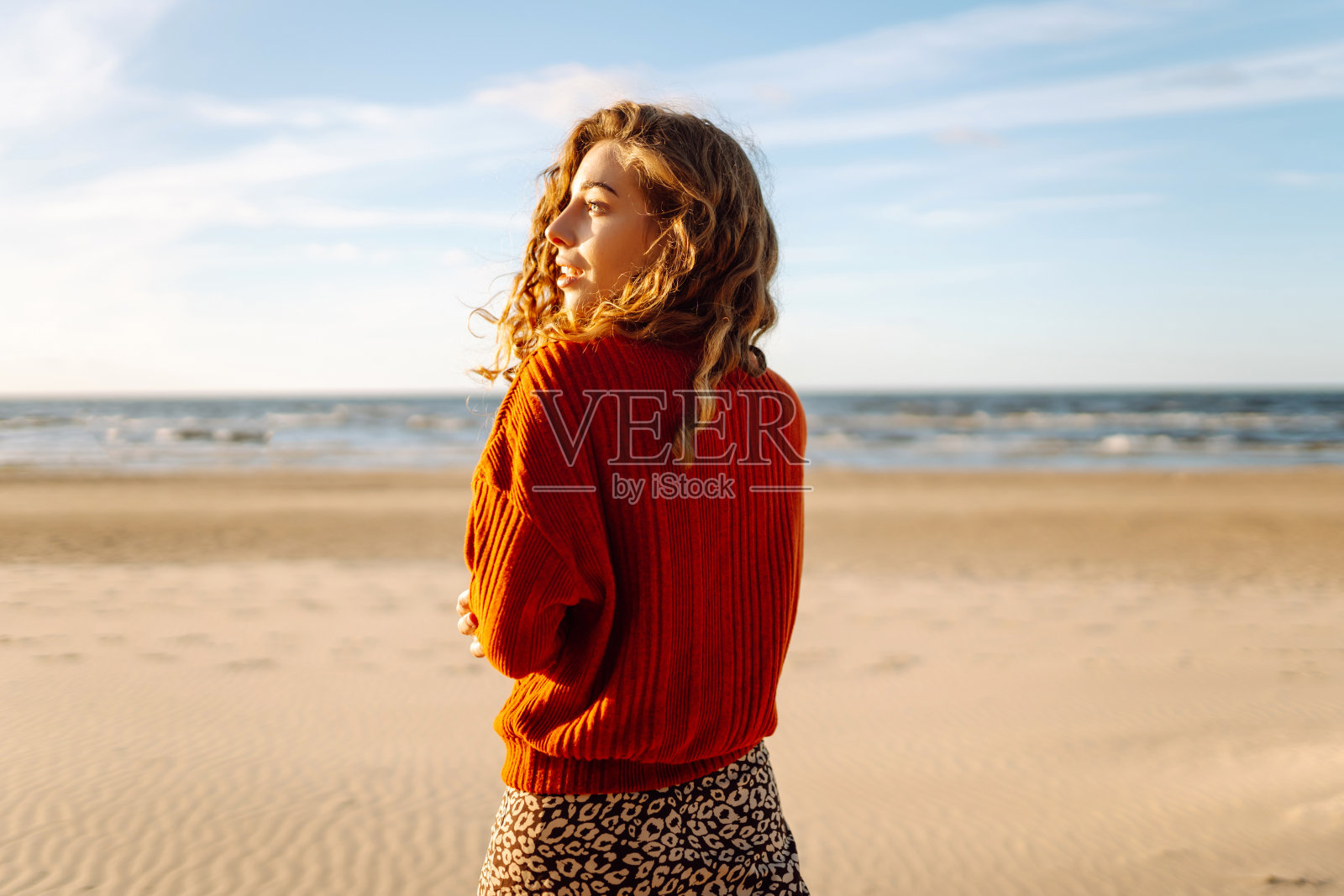 美丽的女人在日落时分走在沙滩上。照片摄影图片
