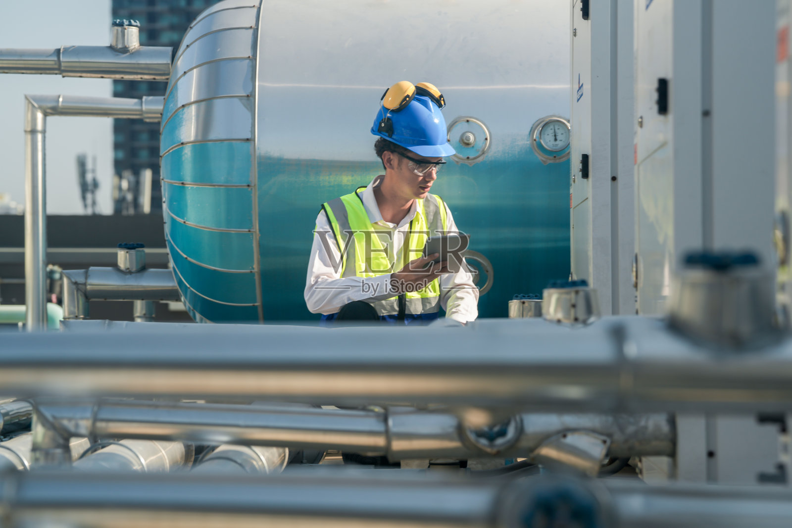 严肃的工程师在商业建筑屋顶用平板电脑检查暖通空调设备。照片摄影图片