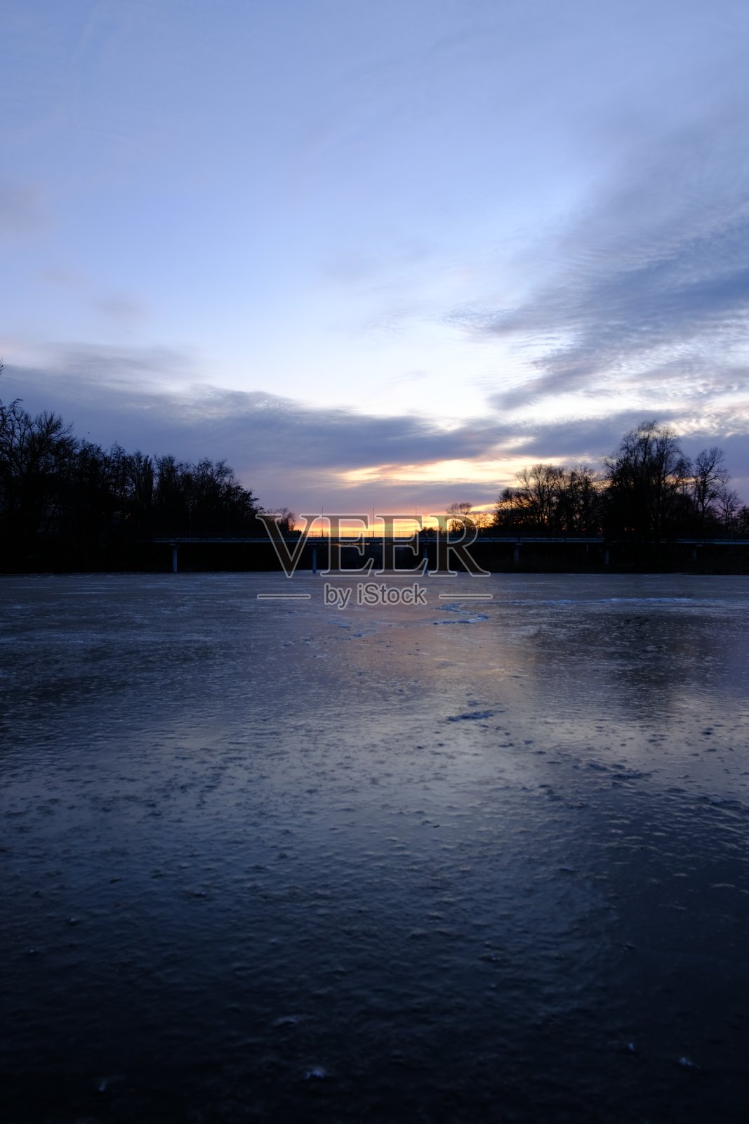 霜冻的粉红色日落在冰冻的河上，一座桥横跨水面，人们走在桥上，从冰冻的河的中心观看照片摄影图片