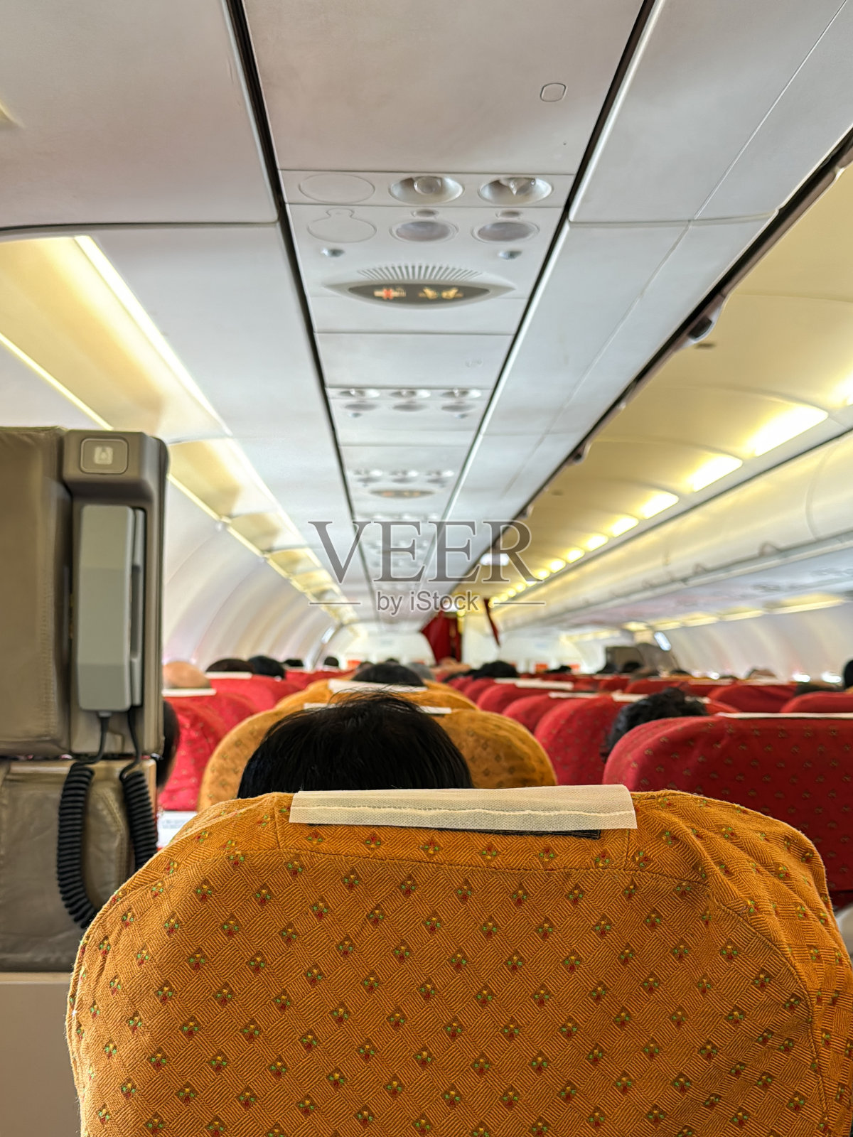 客机经济舱顶置通风控制台特写图像，照明的禁止吸烟和系好安全带标志，乘务员呼叫按钮，后排乘客座椅，缩小视角，聚焦于前景照片摄影图片