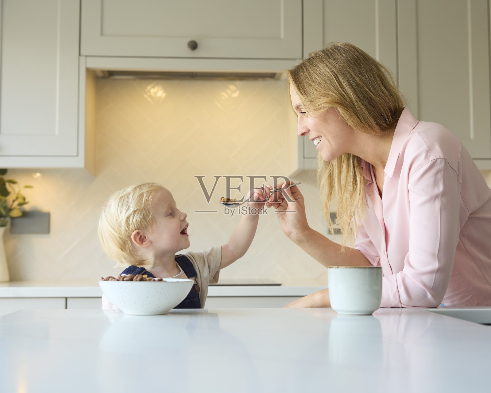 母亲在家鼓励小儿子在厨房吃早餐照片摄影图片