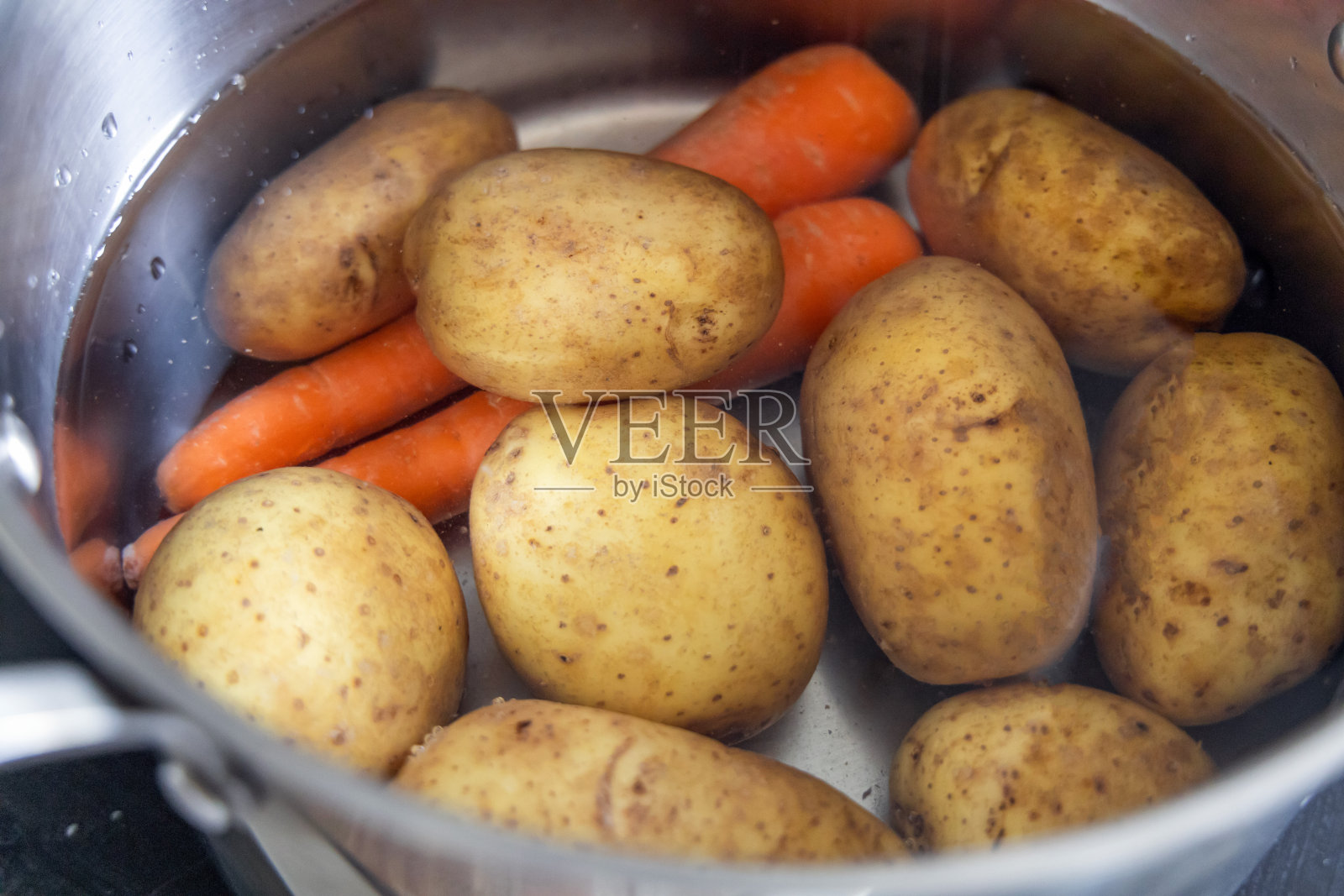 土豆和胡萝卜在炉子上的一锅水里煮。照片摄影图片
