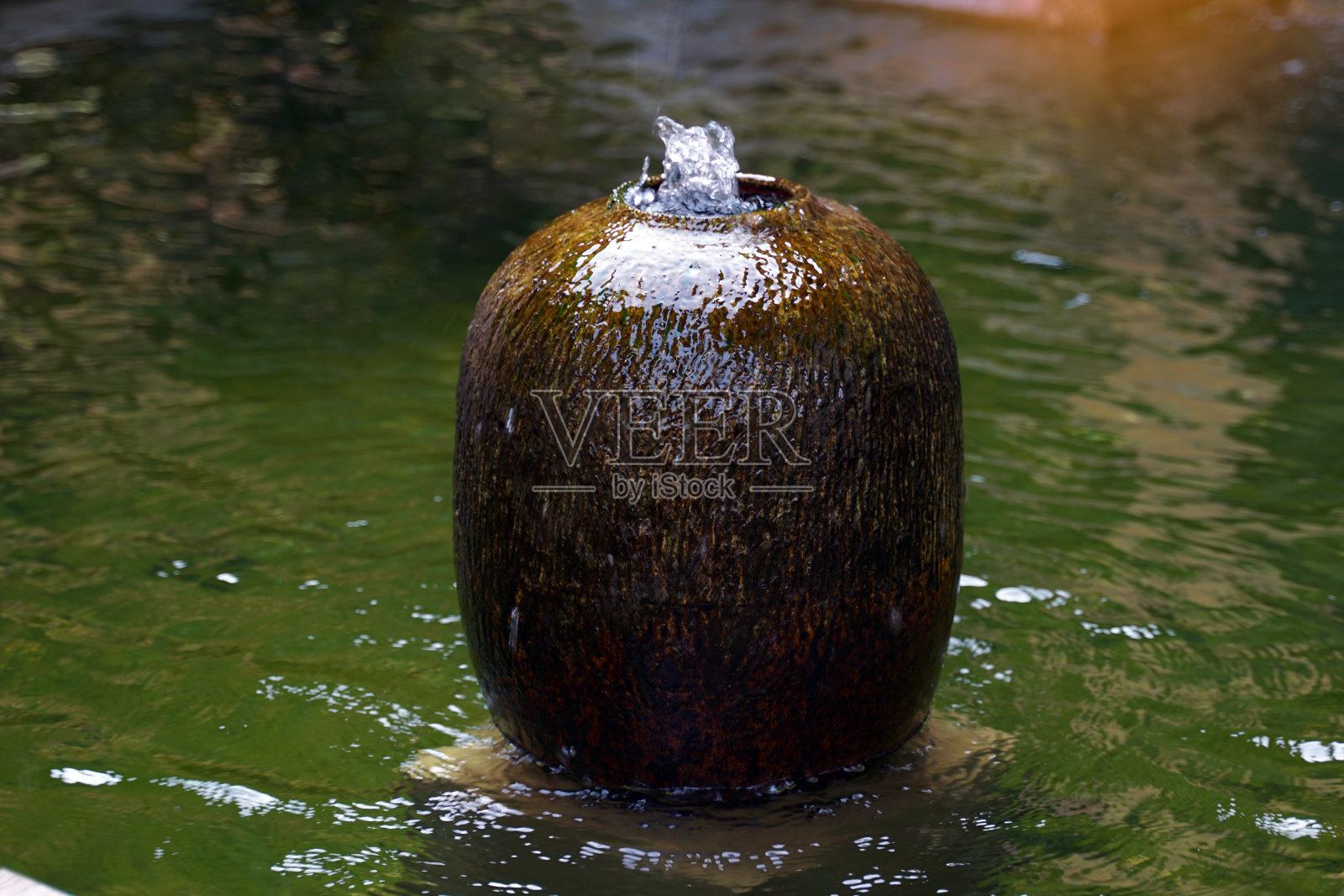 陶瓷喷泉罐安装在房子花园的池塘边。它是装饰房屋和花园的陶器，美观，阴凉，自然，增强风水。照片摄影图片