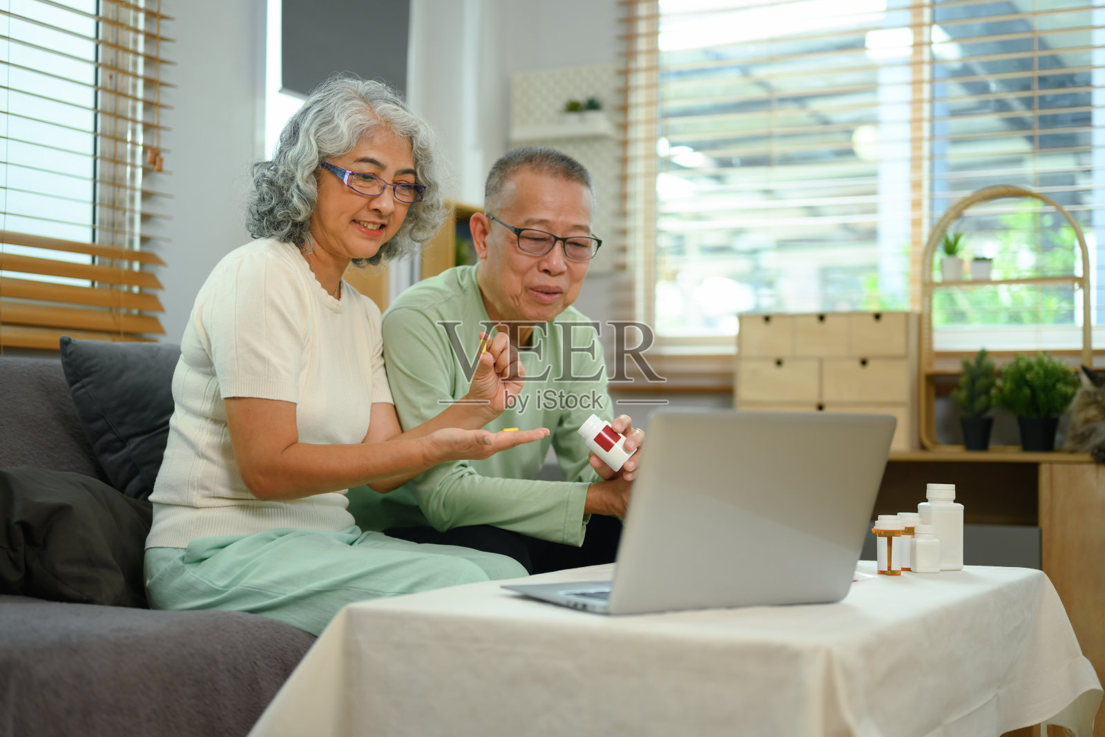 老年夫妇在家里用笔记本电脑视频通话，听取医生关于药片的建议照片摄影图片