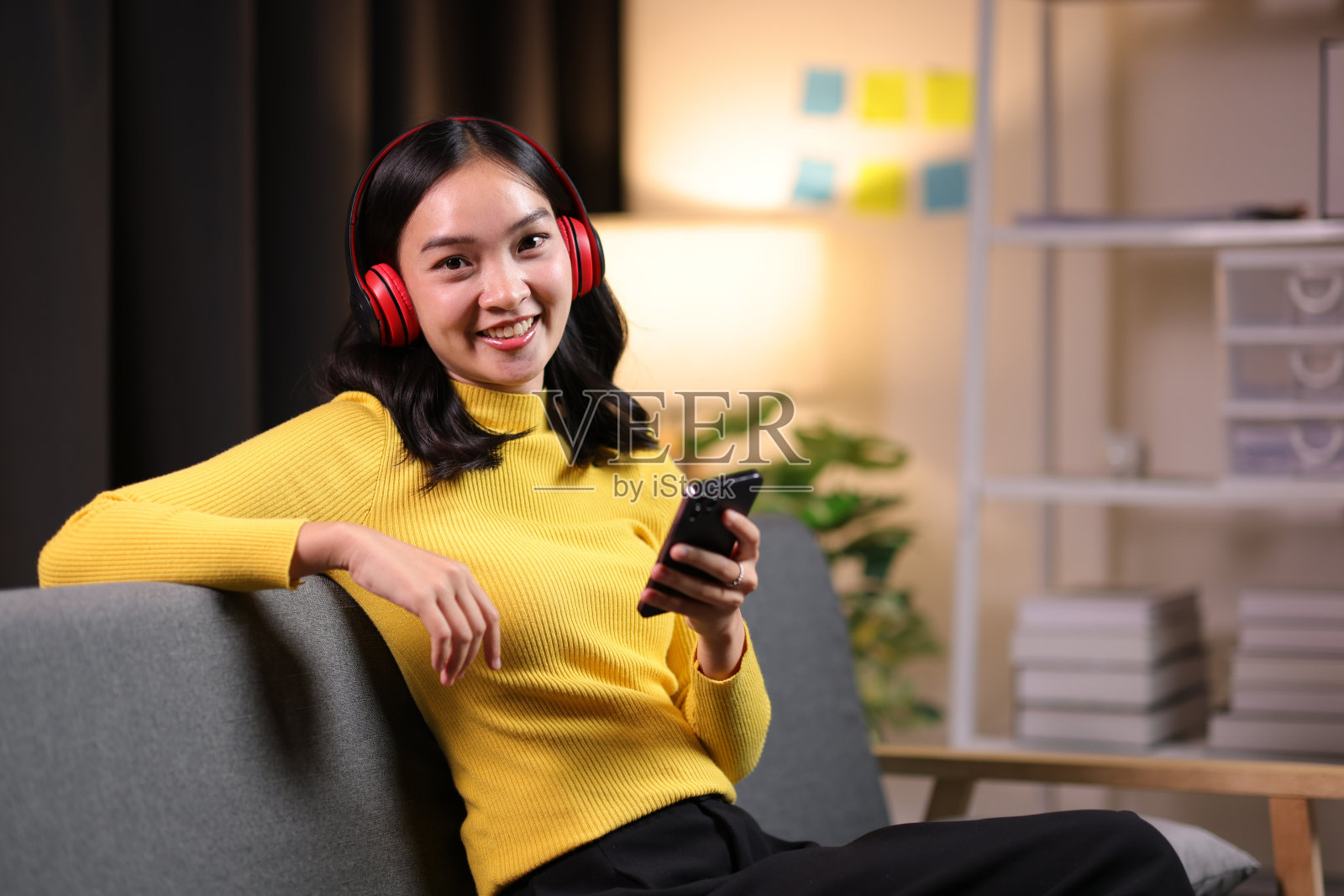 快乐的年轻亚洲女人戴着耳机，听着手机上的音乐，在家里玩得开心。照片摄影图片