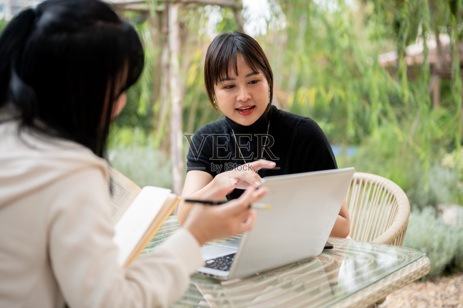 一位亚洲女性和她的同事在花园里远程工作，讨论工作和分享想法。照片摄影图片