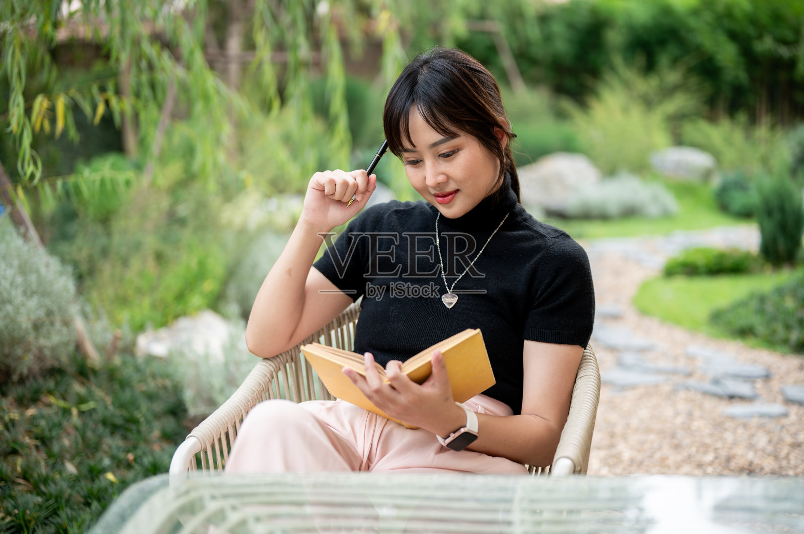 一个积极的亚洲女性在后院放松，在桌子旁看书或写日记。照片摄影图片