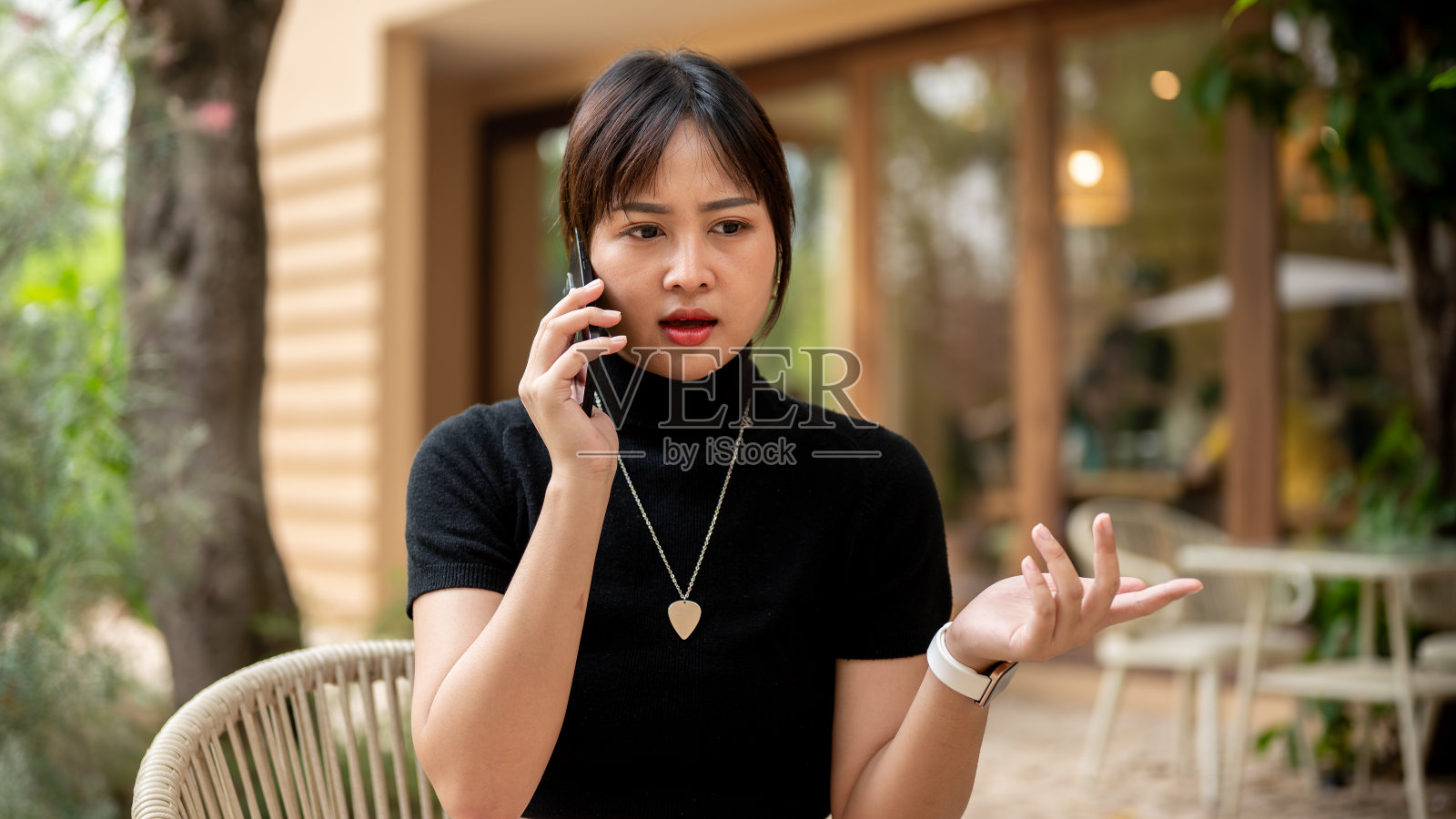 一位亚洲妇女坐在咖啡馆户外的桌子旁，正在严肃地讲着电话。照片摄影图片