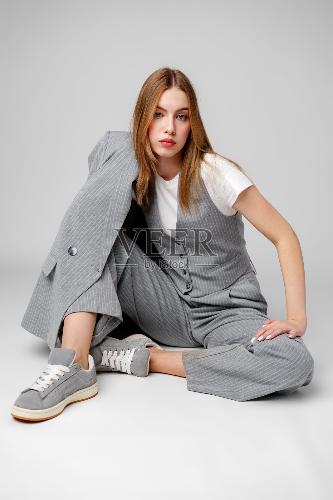 穿着灰色西装的年轻女子坐在演播室的地板上照片摄影图片