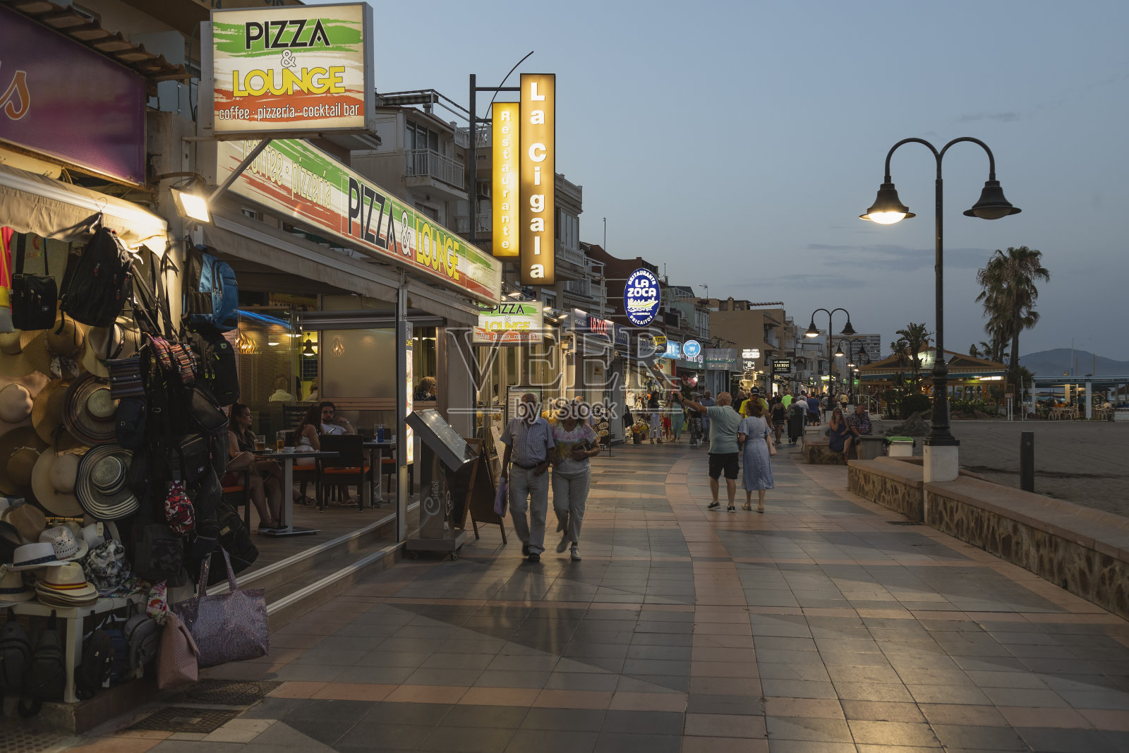 傍晚时分,人们在地中海海滨胜地La Carihuela的林荫大道上散步。照片摄影图片