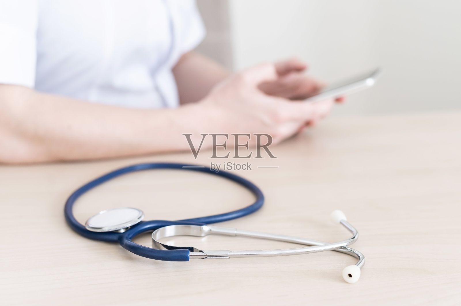 不知名的女医生坐在办公桌前用智能手机写信息。医生手里拿着电话给病人打电话照片摄影图片