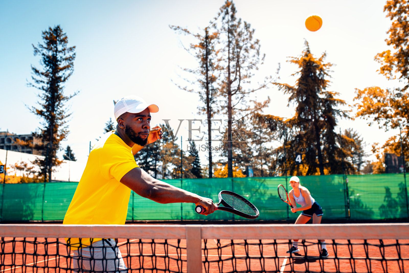 白天，一对夫妇在红土场上打网球。照片摄影图片