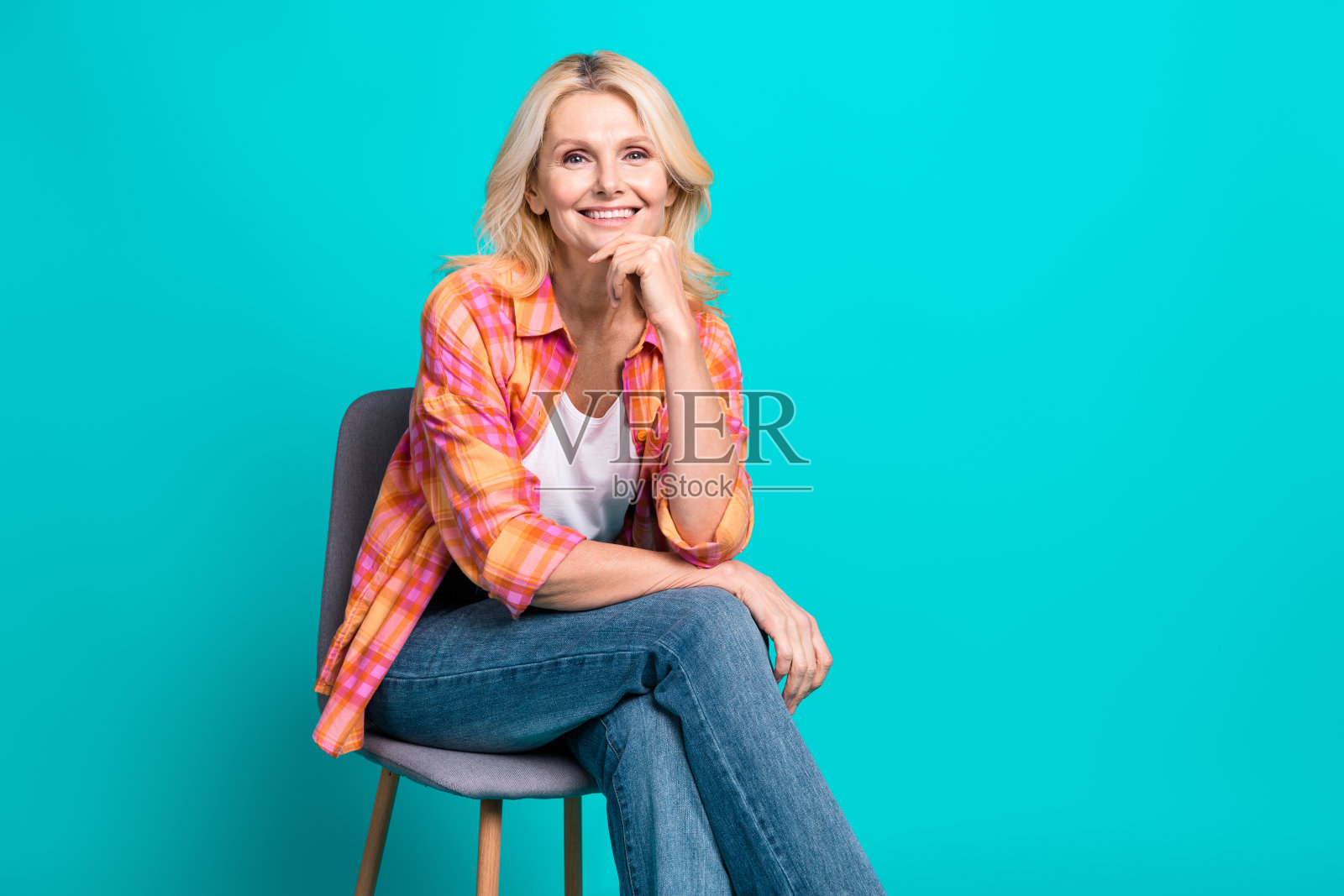 漂亮可爱的高级妇女的肖像，穿着格子时髦的衣服，坐在椅子上，在青色背景上孤立的空间照片摄影图片